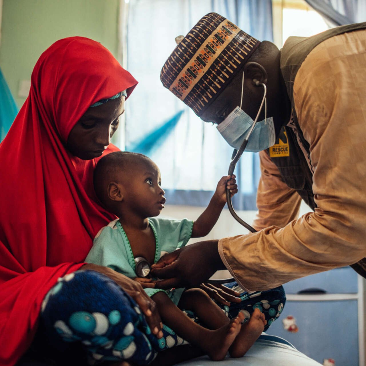 En kvinna i Nigeria håller ett litet barn i famnen samtidigt som en läkare underösker barnet.