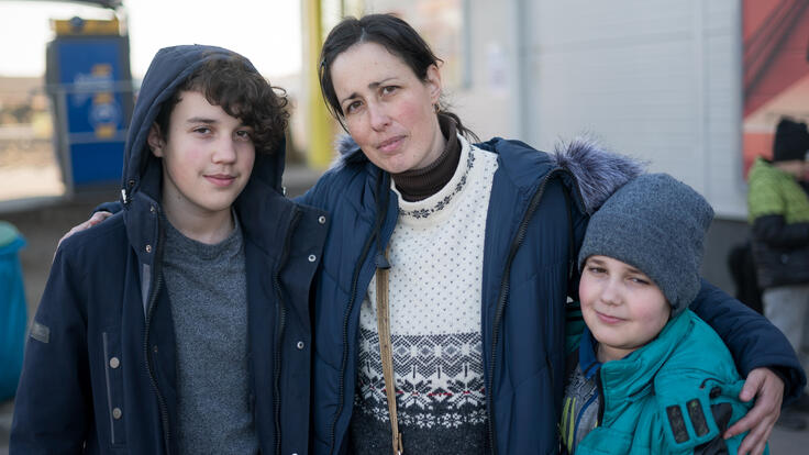 A woman looks at the camera with her arms around her two sons. All are wearing winter clothes.