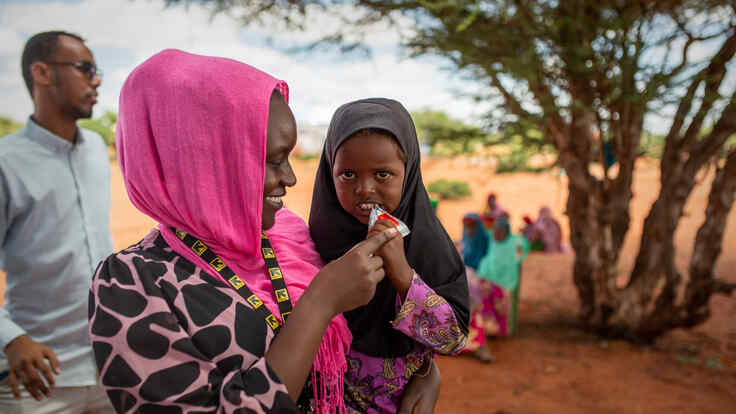 IRC staff with young girl eating PlumpyNut in Olol Village, Somalia