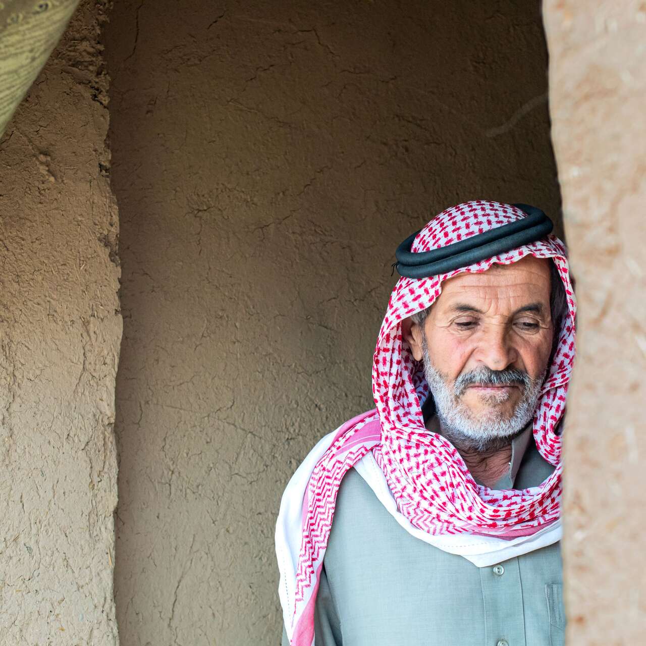 Ein älterer Mann in traditioneller Kleidung steht im Eingang eines einfachen Lehmhauses in Syrien.