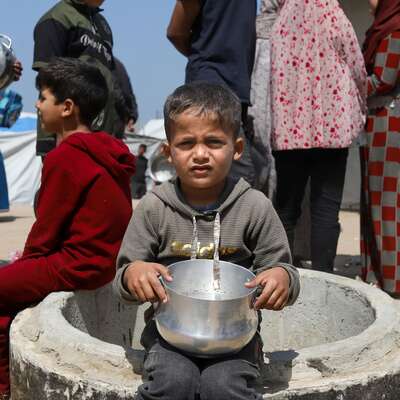 A Gazan child sits with an empty bowl waiting for aid