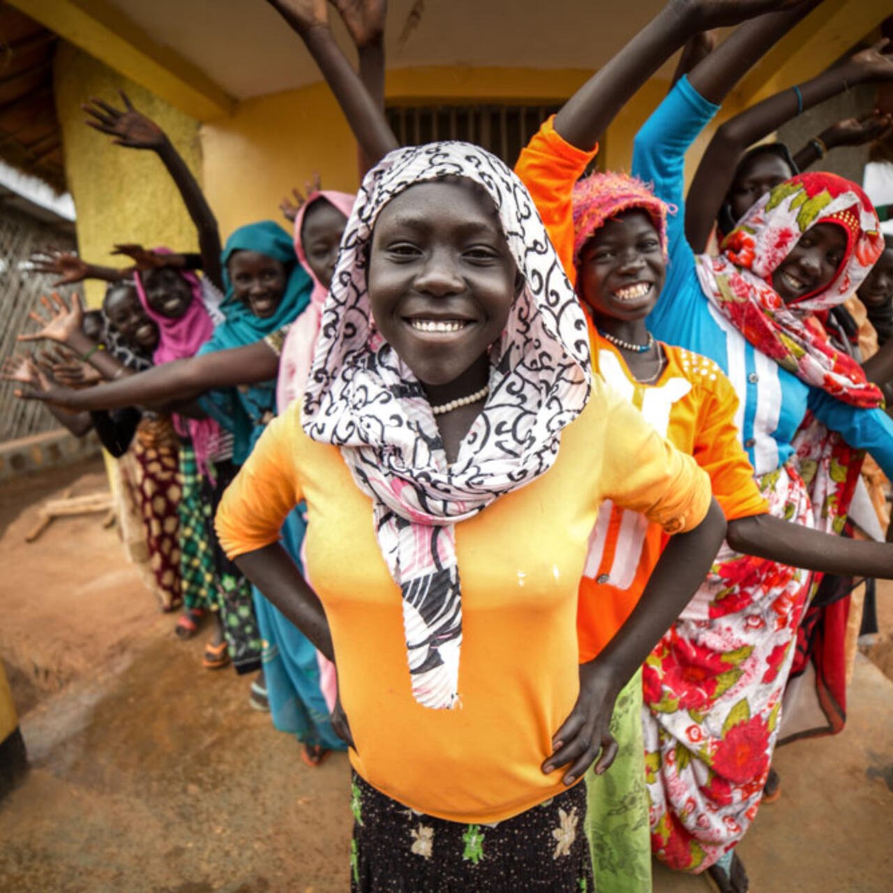 Eine Frau steht im Vordergrund und lächelt, hinter ihr sind mehrere andere, die ihre Arme in die Luft halten.