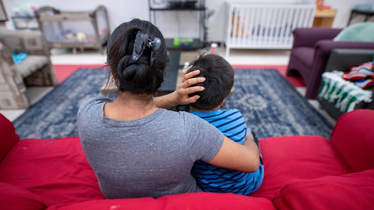 Angelina, an asylum seeker from Guatemala, sits on a red couch with her arms around her son at an IRC Welcome Center in Arizona.