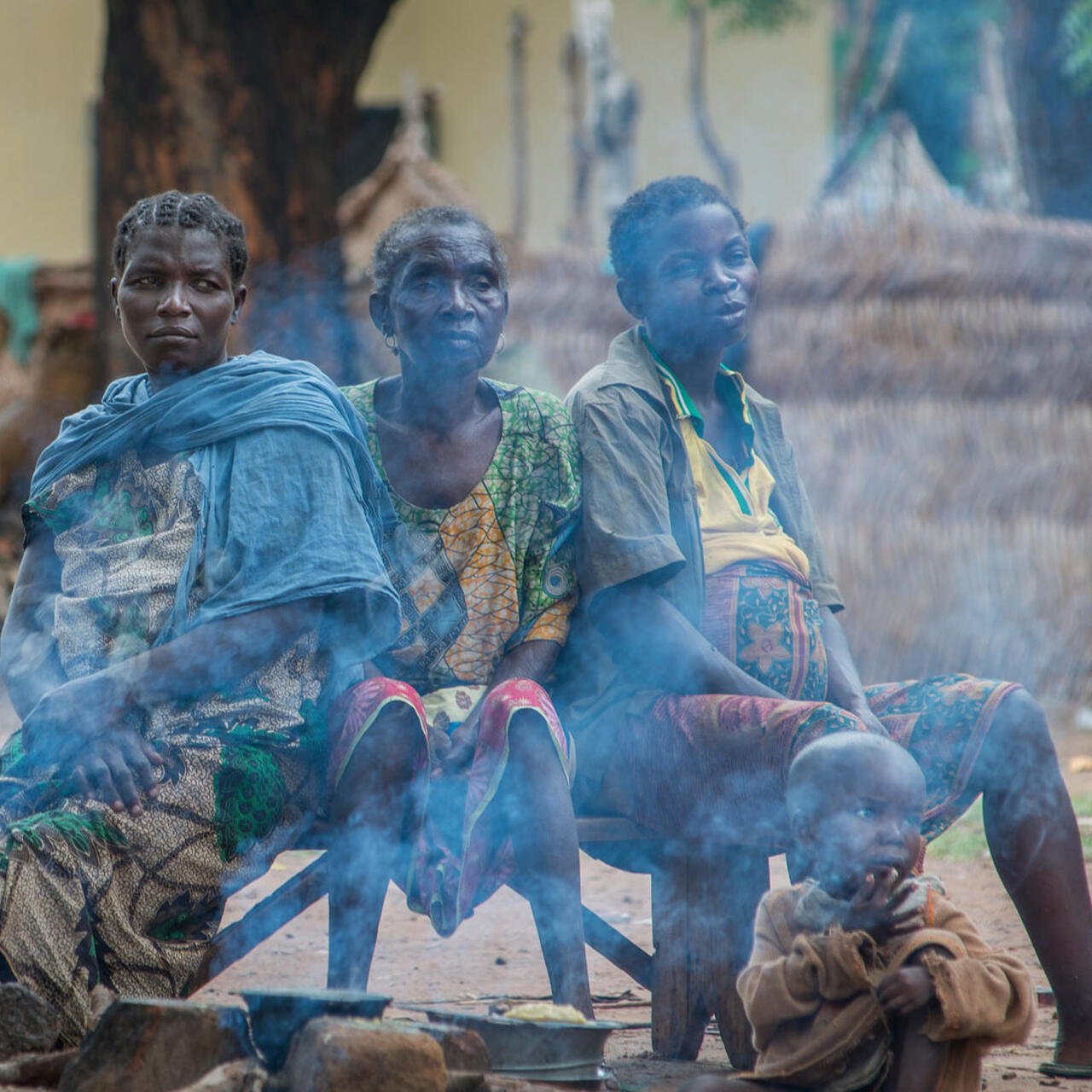 Drei Frauen sitzen an einer Feuerstelle in einem Flüchtlingslager.