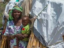 Eine Frau hält ihr Baby auf dem Arm. Im Hintergrund ist ein Zelt zu sehen.
