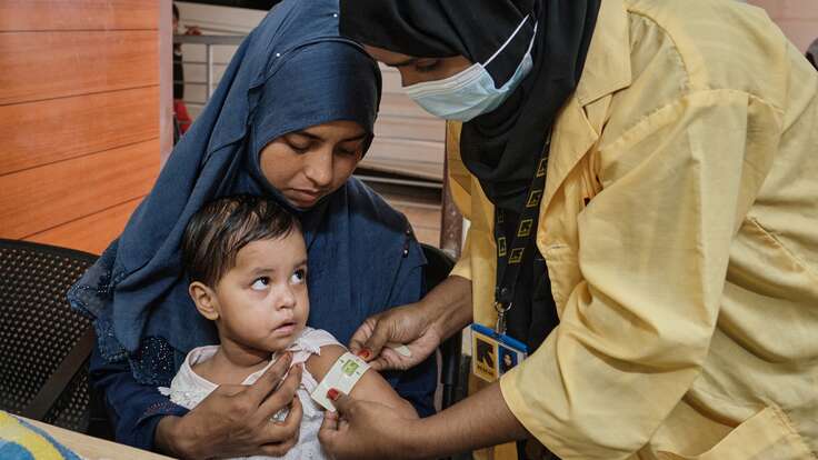An IRC health care worker screens a young Rohingya child for signs of malnutrition.