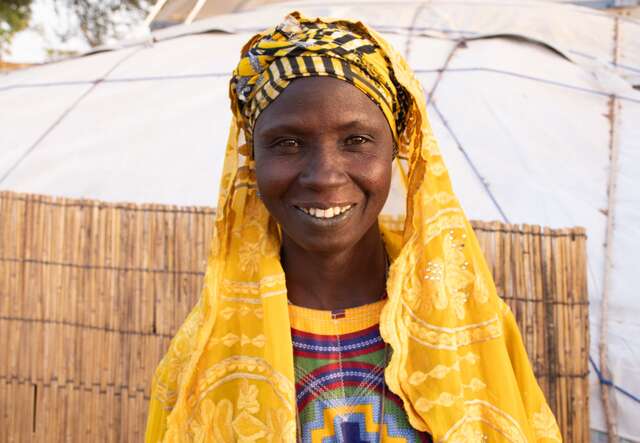 A woman wearing a yellow shawl smiles for a photo in Burkina Faso.